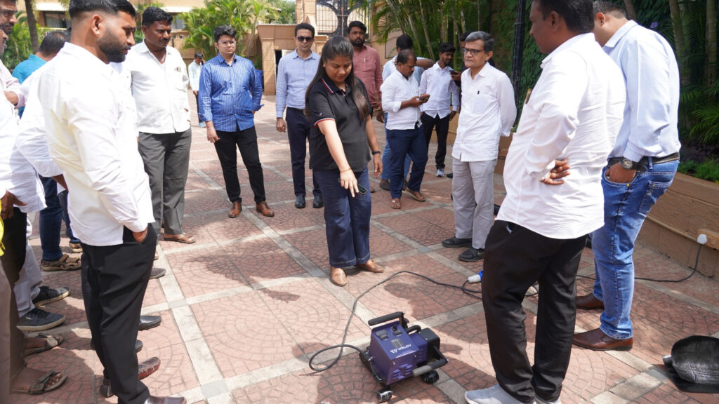 Trainer demonstrating a Weldy geomembrane welding machine to installers and participants during the outdoor practical session at GeoWeld Connect 2025.